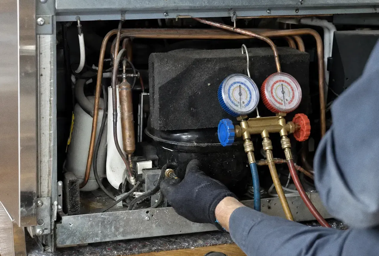 Close view of a compressor, copper suction and discharge lines and a filter drier with a gauge set hanging in front